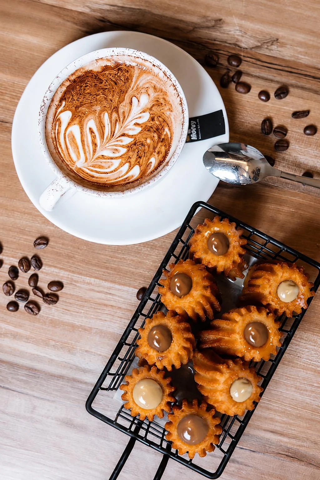 Vista cenital de café con arte latte y porras rellenas sobre mesa de madera