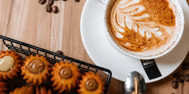 Café con arte latte junto a una cesta de churros rellenos
