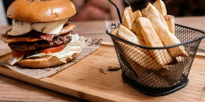 Hamburguesa con bacón y queso junto a una cesta de patatas fritas